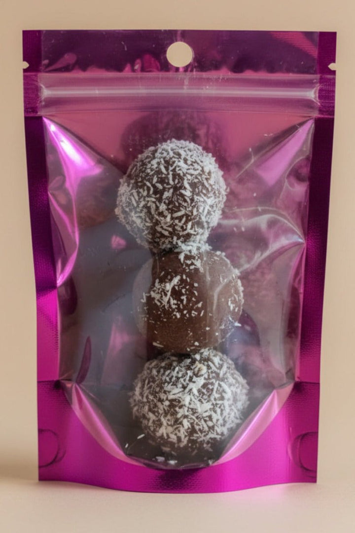 Three chocolate truffles with coconut shavings in a pink reflective packaging bag.